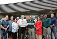 Peterborough mayor Jeff Leal (third from left, front) accepts a symbolic key from Parks Canada's manager of canal operations Chad Buchner for the new Peterborough Visitor Centre during a media event on June 25, 2026, the day before the centre opened to the public, surrounded by city councillors, Parks Canada staff, and two representatives of the Indigenous community. Operated by Peterborough Tourism, the visitor centre is located in the building previously operated by Parks Canada as the Peterborough Lift Lock Visitor Centre until 2020. (Photo: Jordan Lyall / kawarthaNOW)