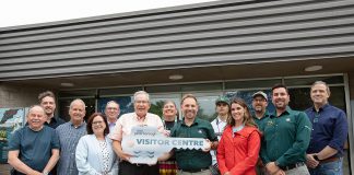 Peterborough mayor Jeff Leal (third from left, front) accepts a symbolic key from Parks Canada's manager of canal operations Chad Buchner for the new Peterborough Visitor Centre during a media event on June 25, 2026, the day before the centre opened to the public, surrounded by city councillors, Parks Canada staff, and two representatives of the Indigenous community. Operated by Peterborough Tourism, the visitor centre is located in the building previously operated by Parks Canada as the Peterborough Lift Lock Visitor Centre until 2020. (Photo: Jordan Lyall / kawarthaNOW)