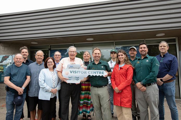 Peterborough mayor Jeff Leal (third from left, front) accepts a symbolic key from Parks Canada's manager of canal operations Chad Buchner for the new Peterborough Visitor Centre during a media event on June 25, 2026, the day before the centre opened to the public, surrounded by city councillors, Parks Canada staff, and two representatives of the Indigenous community. Operated by Peterborough Tourism, the visitor centre is located in the building previously operated by Parks Canada as the Peterborough Lift Lock Visitor Centre until 2020. (Photo: Jordan Lyall / kawarthaNOW)