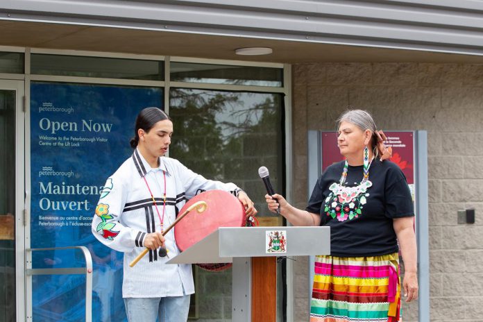 18-year-old Kelvin Boissoneau from Garden River First Nation near Sault Ste. Marie performs as the City of Peterborough's Indigenous relations advisor Shelley Knott holds the microphone during a media event on June 25, 2026 for the opening of the new Peterborough Visitor Centre. The city consulted with Indigenous members of the community to ensure the visitor centre adequately reflects the Indigenous history of the area. (Photo: Jordan Lyall / kawarthaNOW)
