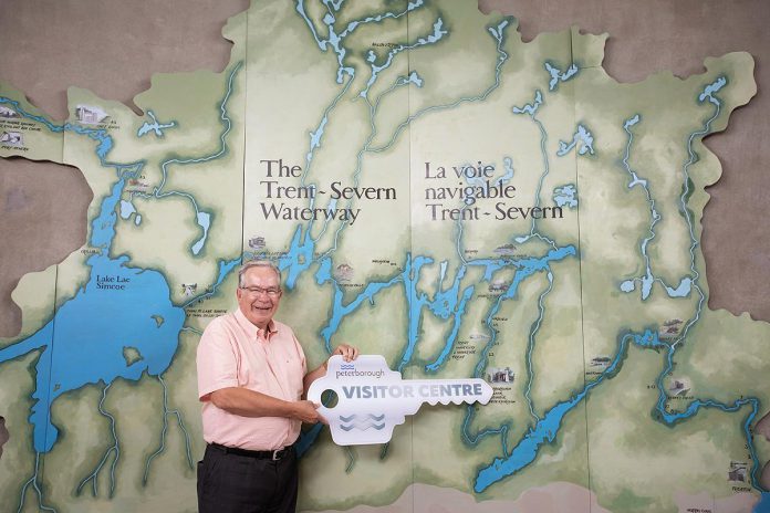 Peterborough mayor Jeff Leal smiles as stands in front of a map of the Trent-Severn Waterway holding a symbolic key for the new Peterborough Visitor Centre during a media event on June 25, 2026. The city has entered into an agreement with Parks Canada to use the building that previously was the home of the Peterborough Lift Lock Visitor Centre until 2020. (Photo: Jordan Lyall / kawarthaNOW)