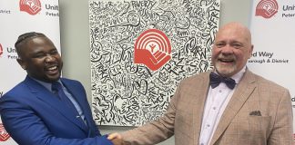 The United Way of Peterborough and District's incoming CEO Jason Seguya shakes hands with retiring CEO Jim Russell during an announcement at the United Way's office on June 18, 2026. The 27-year-old will begin in his new role on July 6, with Russell staying until July 17 to help with the transition. (Photo: Paul Rellinger / kawarthaNOW)
