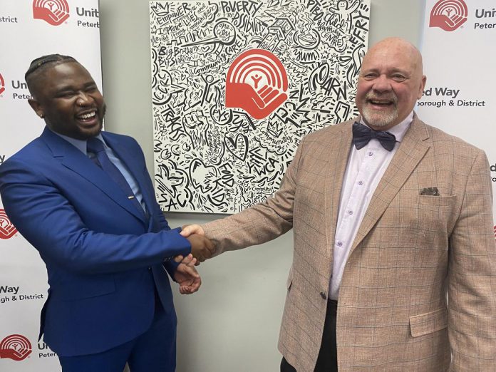 The United Way Peterborough and District's incoming CEO Jason Seguya shakes hands with retiring CEO Jim Russell during an announcement at the United Way's office on June 18, 2026. The 27-year-old will begin in his new role on July 6, with Russell staying until July 17 to help with the transition. (Photo: Paul Rellinger / kawarthaNOW)