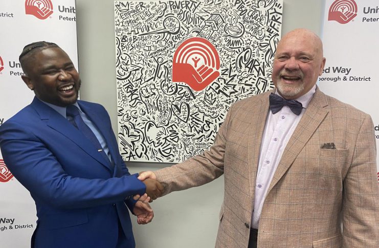 The United Way Peterborough and District's incoming CEO Jason Seguya shakes hands with retiring CEO Jim Russell during an announcement at the United Way's office on June 18, 2026. The 27-year-old will begin in his new role on July 6, with Russell staying until July 17 to help with the transition. (Photo: Paul Rellinger / kawarthaNOW)
