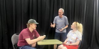 Director Jack van Roosmalen (standing) with actors Eddy Sweeney and Rebecca Birrell during a rehearsal for "Photographic Memory" written by Ron Davies. The 10-minute play, about a man who finds that photos can be as hard as memories to erase after his ex asks him to delete some photos she sent him, is one of 10 plays to be staged as part of the "10 Minute Sunday" short play festival hosted by the Peterborough Theatre Guild on August 9, 2026. (Photo courtesy of D'Arcy Jenish)