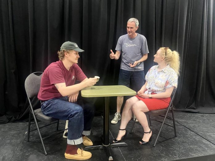 Director Jack van Roosmalen (standing) with actors Eddy Sweeney and Rebecca Birrell during a rehearsal for "Photographic Memory" written by Ron Davies. The 10-minute play, about a man who finds that photos can be as hard as memories to erase after his ex asks him to delete some photos she sent him, is one of 10 plays to be staged as part of the "10 Minute Sunday" short play festival hosted by the Peterborough Theatre Guild on August 9, 2026. (Photo courtesy of D'Arcy Jenish)