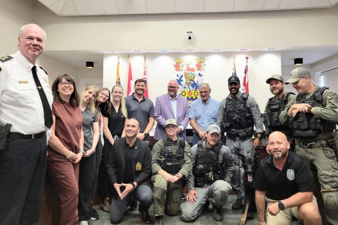 Attendees of a ceremony in council chambers at Victoria Hall on July 28, 2026 to introduce the Cobourg Police Service's new canine team included (standing from left to right) police chief Chris Leather, Tammy Martell, Dr. Ronnie Moore, Hailey Button, and Caroline May of Port Hope Veterinary Emergency Clinic and Services, Justin McClenaghan of Justin's Pet Store, police services board chair Adam Bureau, retired sergeant Don Missen who led Cobourg's previous canine unit, constable Amrit Gill and K-9 Atos, Brandon Regeling and Tyson Chapman of Halton Police Service and (kneeling from left to right), police services board vice-chair Sean Graham, constable Erin Toth of Halton Police Service, constable and canine trainer Jay Hall of Guelph Police Service, and Jesse Mcinroy of Belleville Police Service. (Photo courtesy of Cobourg Police Service)