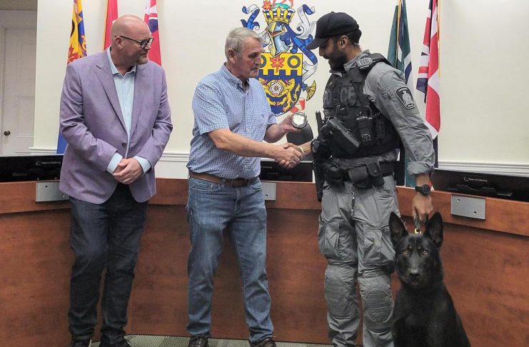 Cobourg police service board chair Adam Bureau (left) and retired sergeant Don Missen, who led the Cobourg police's former canine unit from 1997 to 2003, presented Constable Amrit Gill and German shepherd Atos with the K-9 badge at a ceremony during the police service board's meeting in council chambers at Victoria Hall on July 28, 2026. (Photo courtesy of Cobourg Police Service)