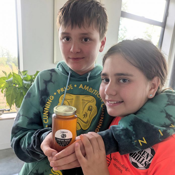 Empire Beez founder Sebastian Smith holding a jar of honey with his arm around his sister Eloise. Along with Sebastian's friends Owen Musson and Penelope McEvoy, the pair are working together to run the small business that raises awareness around honeybees and installs community beehives. (Photo courtesy of Blythe Weber)