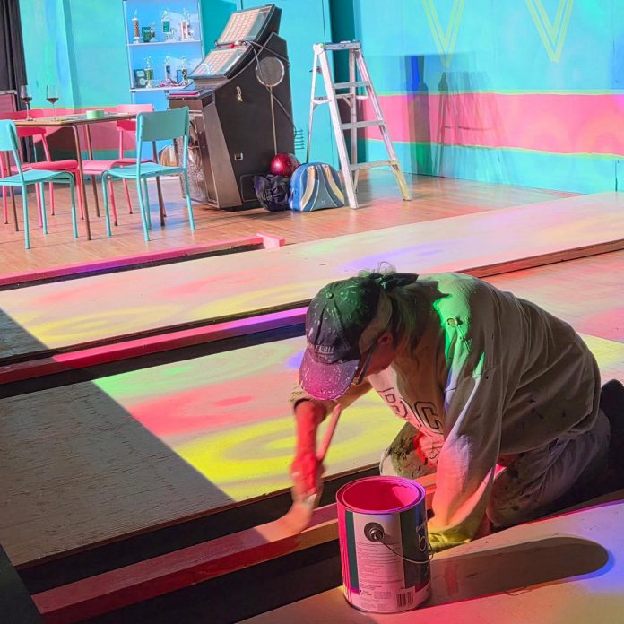 Kim Hone works on a retro bowling alley set on the stage of Globus Theatre in Bobcaygeon for the world premiere of Bradley Austin's comedy "Sore Losers" from July 15 to 25, 2026. (Photo: Globus Theatre / Facebook)