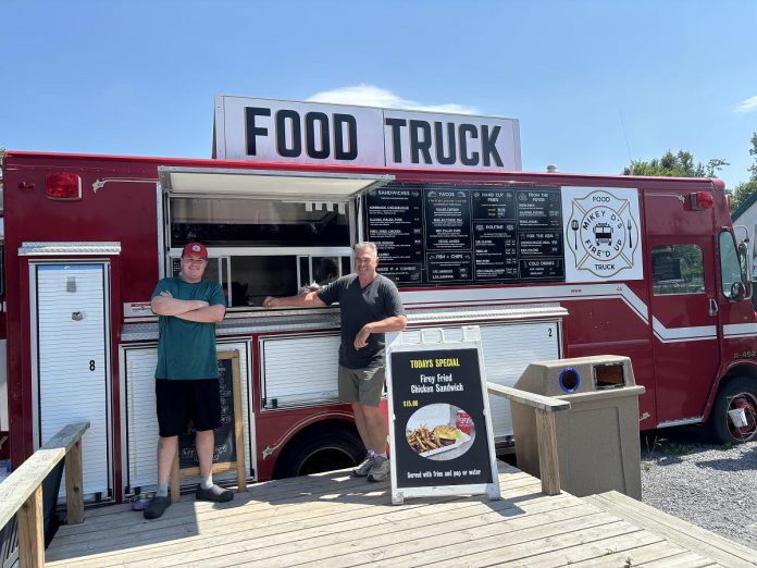Mikey D's Fire'd Up Food Truck owner Mike Del Mastro (right) with nephew and employee Dave Matheson pictured outside of the restored fire truck on Highway 28 in Apsley. Located where the Creekside Music Festival was previous located, Mikey D's Fire'd Up Food Truck is known for itsS fish tacos made with beer-battered cod. (Photo: Megan Gallant / kawarthaNOW)