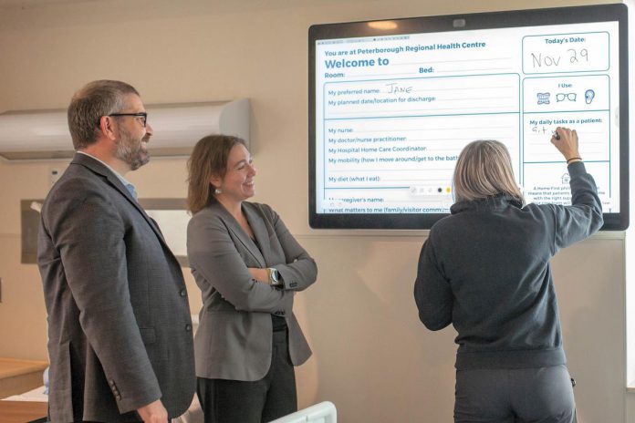 Peterborough Regional Health Centre (PRHC) vice president and chief nursing executive Noel Bennett (left) and president and CEO Dr. Lynn Mikula watch as occupational therapist Beth Morgan uses a digital communication board within the regional hospital's Reactivation Care Centre in December 2024. (Photo courtesy of PRHC)
