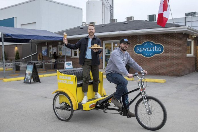 The Amazing Race Canada host Jon Montgomery holds an ice cream cone and a tray of butter tarts outside of Kawartha Dairy in Bobcaygeon in the fifth episode of season 12 of the reality TV series. In the episode, teams will be delivering iconic snacks to destinations around the historic village, which is celebrating its 150th birthday this year. (Photo: Bell Media)