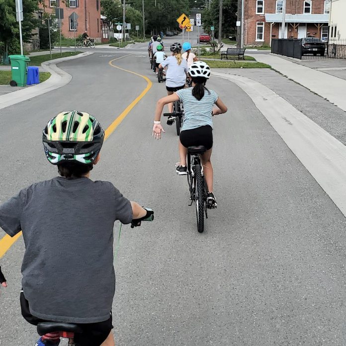 Campers with GreenUP's Urban Bike Adventures Camp use hand signals as they come to a stop along the Bethune Street bicycle boulevard. It's one of the bike skills they learn as part of the week-long camp that lets kids aged nine to 12 explore Peterborough via its trails and cycling infrastructure, all while under the guidance of trained cycling educators. (Photo: Brett Throop / GreenUP)
