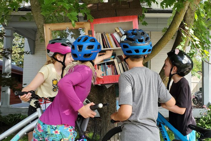 Kids look for a summer read at a little free library on the front lawn of a Maria Street home. Visiting one of these tiny libraries is one way to complete the Summer Ride Club's "ride to read" challenge, one of nine cycling challenges kids and families complete over the course of the summer. (Photo: Brett Throop / GreenUP)