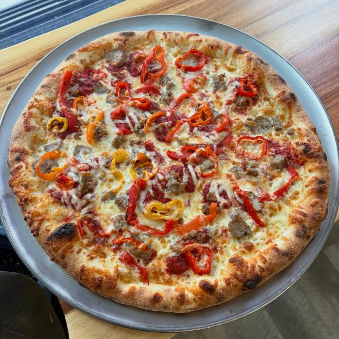 Zach Washburn turned his pizza making hobby into a business by selling weekly "porch pizzas" from his home before eventually building a pizza cart and later opening Pies by Zach in downtown Millbrook. The pizzeria adds a new pizza to the menu every other week, liked this pizza with a garlic base, mozzarella, garlic and chive sausage, fire-roasted red peppers, banana peppers, and a sprinkle of the in-house asiago and provolone blend. (Photo courtesy of Pies by Zach)