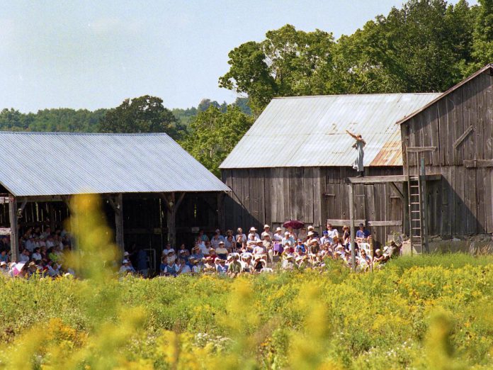 An audience watches a performance on the barnyard stage at Winslow Farm, the rural backdrop that has shaped 4th Line Theatre's outdoor productions for more than three decades. The theatre company defines their plays as "environmentally staged," blurring the line between the stage and the thoughtfully cared-for natural world surrounding their performances. (Photo: Wayne Eardley, Brookside Studio)