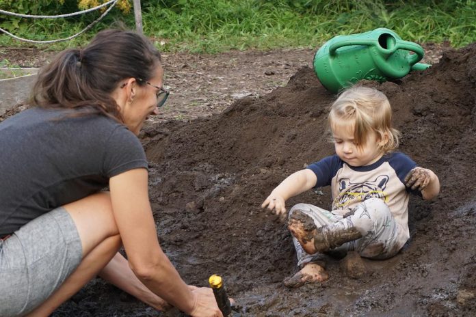 A toddler caked in mud on a mound of topsoil at GreenUP Ecology Park's pop-up Mud Pit during Family Night on August 27, 2026. The nature-based pop-ups helped GreenUP learn more about the interest and engagement levels of visitors in hopes of implementing more permanent outdoor activity environmental centres. (Photo: Alex Karn / GreenUP)