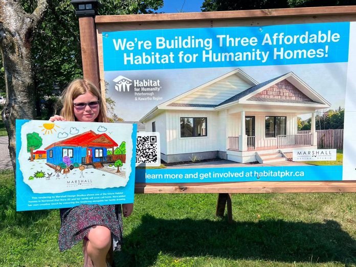The daughter of a future homeowner of one of the three single-family homes in Norwood being constructed by Habitat for Humanity Peterborough & Kawartha Region (Habitat PKR) displays her artwork of the new home designed by Marshall Design Studios during a ground-breaking ceremony on July 14, 2026. Habitat PKR is inviting company teams and individuals to participate in building the homes during Women Build '26 from September 21 to 24. (Photo: Habitat PKR)
