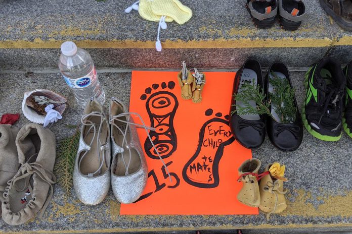 Children's shoes, toys, and offerings on the steps of Peterborough City Hall in June 2021 as part of a community memorial created in response to the discovery of the remains of 215 Indigenous children buried at the former Kamloops Indian Residential School in British Columbia. As well as remembering and honouring those lost to residential schools and the thousands of survivors, National Day for Truth and Reconciliation is a day for Canadians to educate themselves about the heritage, culture, stories, and experiences of First Nations, Inuit, and Métis peoples. (Photo: Bruce Head / kawarthaNOW)